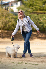 attractive middle-aged blond woman walking with dog in summer city