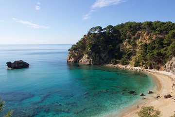 Fototapeta premium Alonaki beach in Preveza near Parga with sandy beach and a big rock in the blue sea, in a pine trees forest. Background view of horizon and blue sky