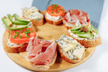 Traditional Italian bruschette snack on a wooden plate on a white wooden table and gray napkin. Mini sandwich mix