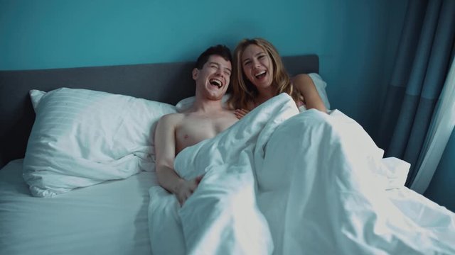young couple is lying in bed, looking under the blanket at the man and laughing. problems in sex. problems in marriage. prank. funny video advertising