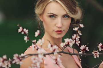 Portrait of young beautiful blonde woman in pink dress near blooming tree with white flowers on a...
