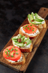 Assorted vegan bruschette snack on a wooden chopping board on a dark textured table. Mini sandwich mix. Top view, close up