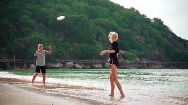 Slow-motion footage of two young women throwing a frisbee at the tropical beach on a sunny day.