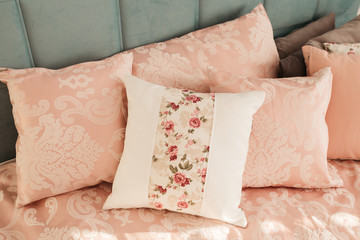 Fototapeta na wymiar Different pillows on the bed. Close-up pink bedding sheets and pillow on light wall room background. Closeup of new bed comforter with decorative pillows. 