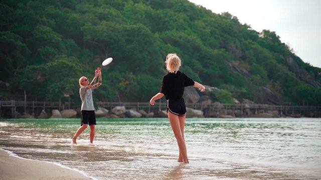 Slow-motion footage of two young women throwing a frisbee at the tropical beach on a sunny day.