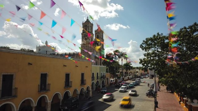 Panning to the right time lapse of flags waving in front of the Catedral de San Gervasio in Valladolid, Yucatan, Mexico.