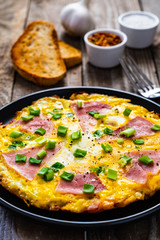 Breakfast - scrambled eggs with ham and vegetables on wooden background