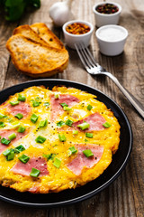 Breakfast - scrambled eggs with ham and vegetables on wooden background