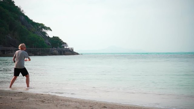 Slow-motion footage of woman throwing a frisbee at the tropical beach on a sunny day.
