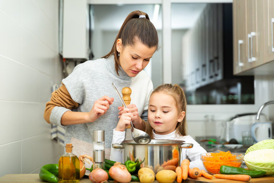 Daughter helping cooking soup and mother add pepper to pan