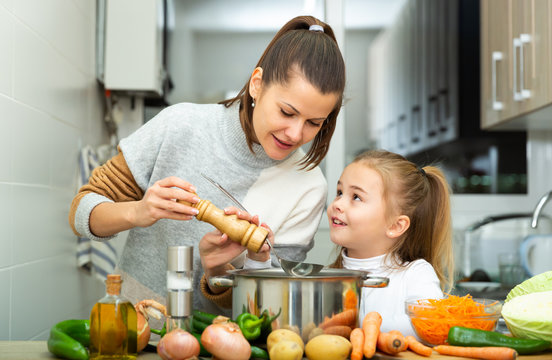 Daughter helping cooking soup and mother add pepper to pan
