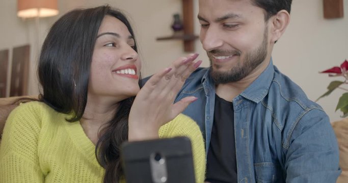 Playful couple take selfies and make funny faces as they take photos on their smart phone mobile device seated at home on valentine's day date. 60fps slow-motion handheld 