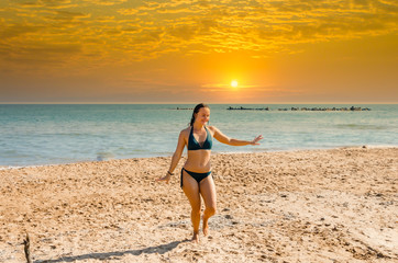 Fototapeta premium A girl in a swimsuit dancing on the beach near the sea in summer.