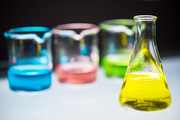 Yellow chemical liquid containing in flask with lab glassware on black background, la research and...