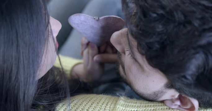 Indian couple intimate as they share together up close and personal a wooden heart shape together seated indoors on a couch in each other's arms. 60fps slow-motion hand-held