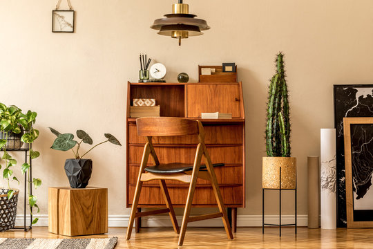 Retro interior design of living room with wooden vintage bureau, design chair, plants, cacti, maps, brown pendant lamp and elegant personal accessories. Stylish home decor. Beige wall. Template. 