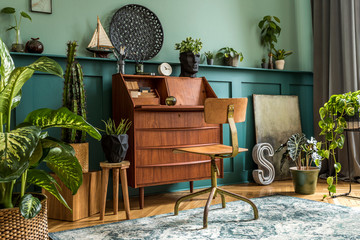 Modern and retro composition of home office interior with wooden cabinet, chair, plants, decoration and elegant personal accessories. Stylish vintage concept of home decor. Wood panelling. Template.
