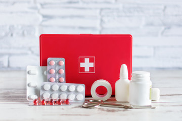 First aid kit red box with medical equipment and medications for emergency on white wooden...