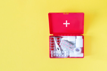 First aid kit red box with medical equipment and medications for emergency top view on pastel yellow background.