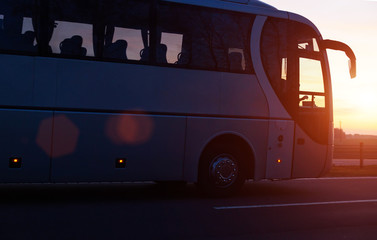 Modern comfortable passenger bus against the background of the orange sky with sunset rides on the...
