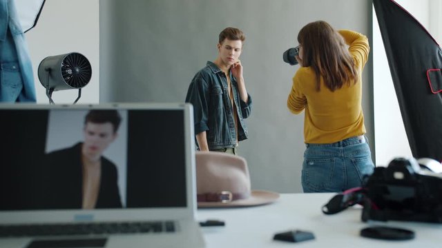 People model and photographer in studio during photoshoot working indoors, guy is posing while girl is taking pictures with modern camera. Youth and creativity concept.