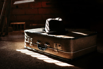 Old, retro suitcase with black hat on it and black background. Travel concept