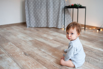 Little cute one year old girl sitting on floor at home.