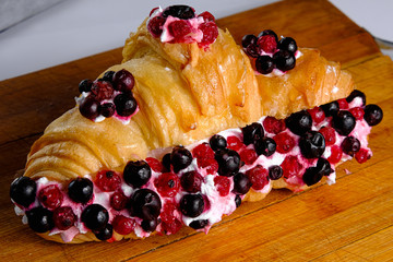 Croissant sandwiche with berries on a wooden background