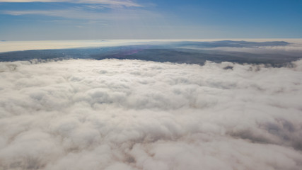 Landscape over the clouds in foggy weather. Hills of buildings in foggy weather. The drone and the top of the fog layer.