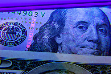 Extreme closeup on dollar banknote under ultraviolet light. Benjamin franklin portrait being inspected. Money falsification concept background.