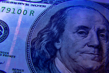 Extreme closeup on dollar banknote under ultraviolet light. Benjamin franklin portrait being inspected. Money falsification concept background.