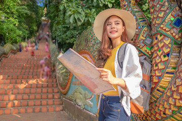 Smiling woman traveler in doi suthep temple chiangmai landmark in thailand holding world map with backpack on holiday, relaxation concept, travel concept