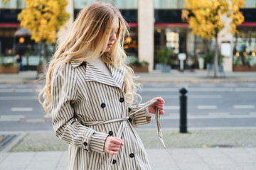 Gorgeous blond girl in stylish trench coat walking around city street