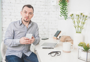 Serious man working using laptop with smartphone at home