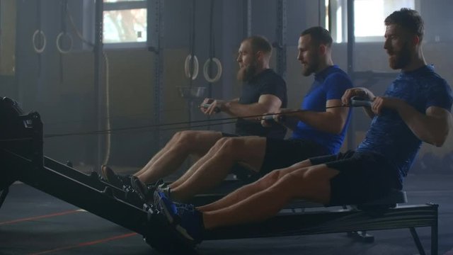 Young fitness three man make exercise on rowing machine in gym. 3 Male athlete training at exerciser in health club. Men with perfect fitness body in sportswear. 