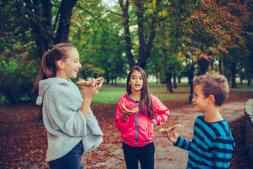 Three happy children laughing, talking and eating pizza outdoors