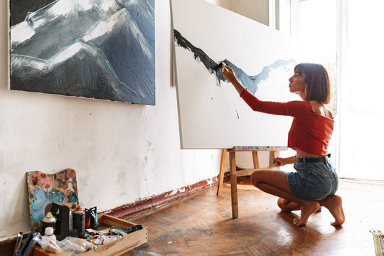 Portrait of young woman using painting tools while drawing in studio
