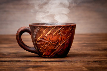 Brown clay cup with hot tea on a wooden table_