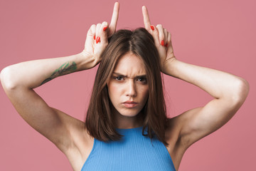 Image of angry brunette woman holding fingers on her head like devil horns