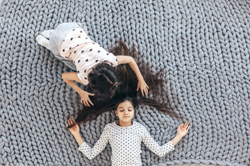 Children in sleepwear lying down and playing with each other on chunky giant woolen blanket