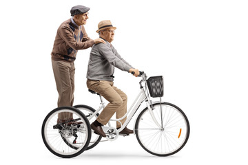 Obraz premium Elderly man riding a tricycle with another elderly man standing behind
