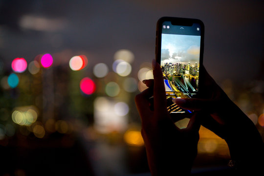 A girl takes pictures of the night city from a skyscraper in Singapore and Kuala Lumpur on her phone