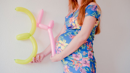 A close up photo of a pregnant young woman holding in her hands the week number thirty four (34) next to her belly in a beautiful dress. Photos of a pregnant woman in the third trimester expecting.
