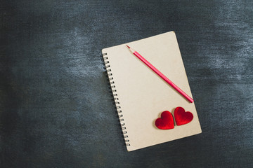 Two red hearts and red color pencil on brown notebook on black wooden background, dark tone, valentine concept.