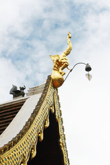 Fototapeta na wymiar Golden naga and bells hanging on Art Roof of Buddhist temple with blue sky in Thailand