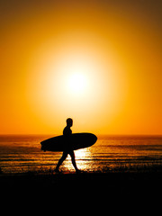 male surfer walking with his table in a sunset