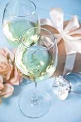 Two glasses with white grape wine with roses and gift box on the background. Romantic dinner concept.
