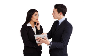 A young businessman is reprimanding a young business woman. He is looking at her. He is holding a tablet. He is pointing at it. She is looking at him.
