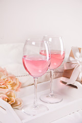 Two glasses with pink grape wine with flowers and gift box on the background. Romantic dinner concept.