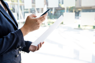 Business woman used smartphone and holding paper at the office room, Setting challenging business goals and ready to achieve the target concept
